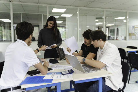 Groupe détudiants en salle détude collaborant autour dune table avec ordinateurs et documents.