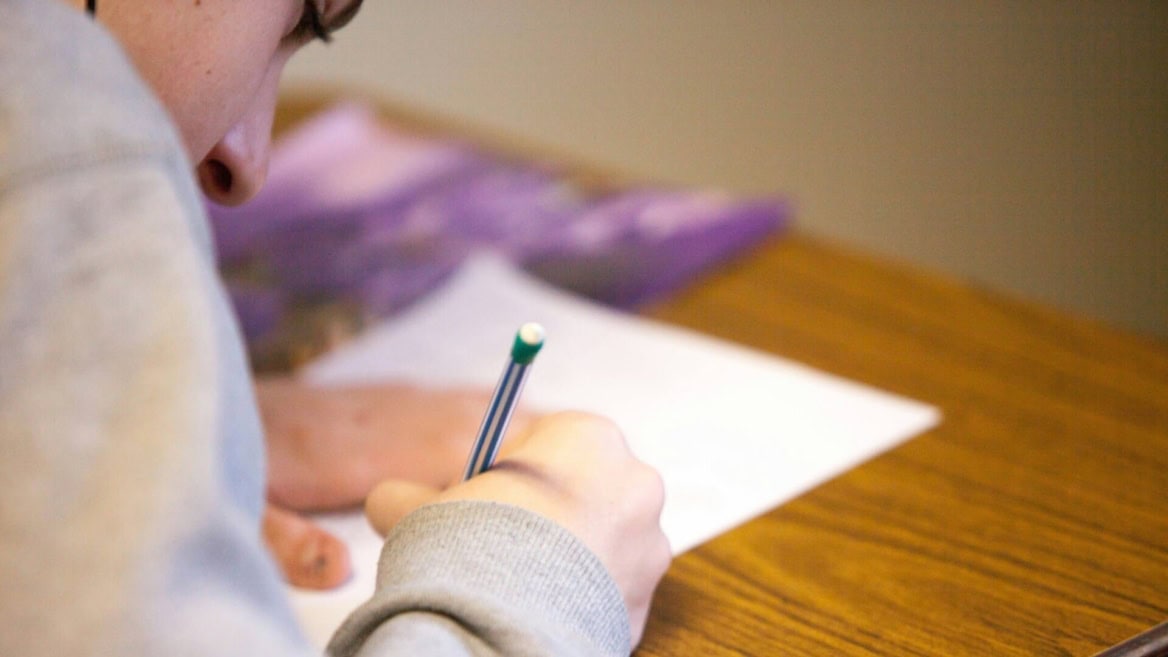 Personne écrivant au crayon sur papier, gros plan sur une table en bois.