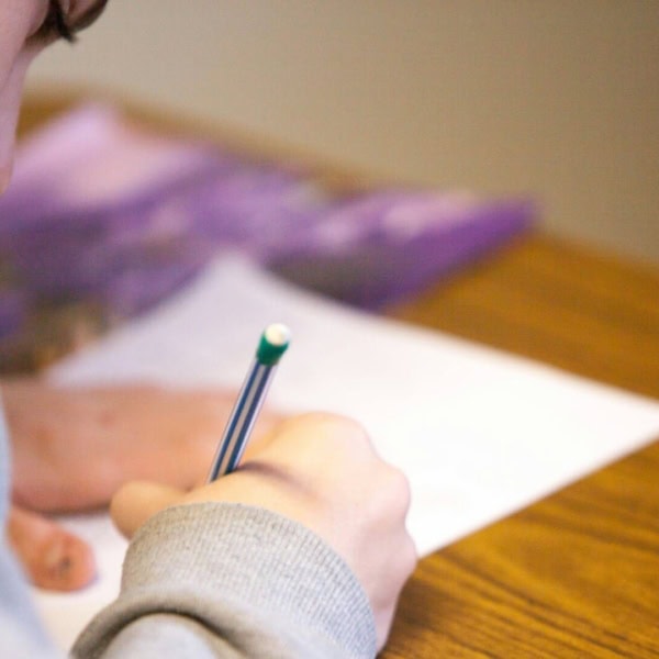 Personne écrivant au crayon sur papier, gros plan sur une table en bois.