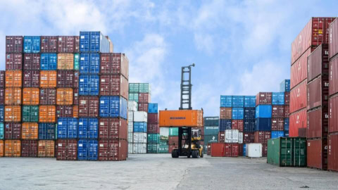 Parc de conteneurs portuaire, engin de manutention soulevant conteneur orange, piles empilées.