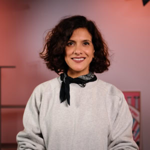 Portrait femme souriante en bandana noir et sweatshirt gris, micro-cravate en studio.