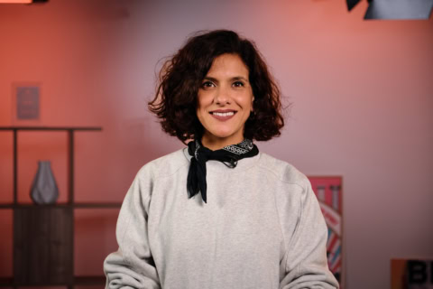 Portrait femme souriante en bandana noir et sweatshirt gris, micro-cravate en studio.