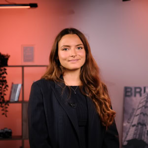 Portrait professionnel dune femme en blazer, micro-cravate, fond studio chaleureux.