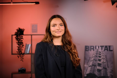 Portrait professionnel dune femme en blazer, micro-cravate, fond studio chaleureux.
