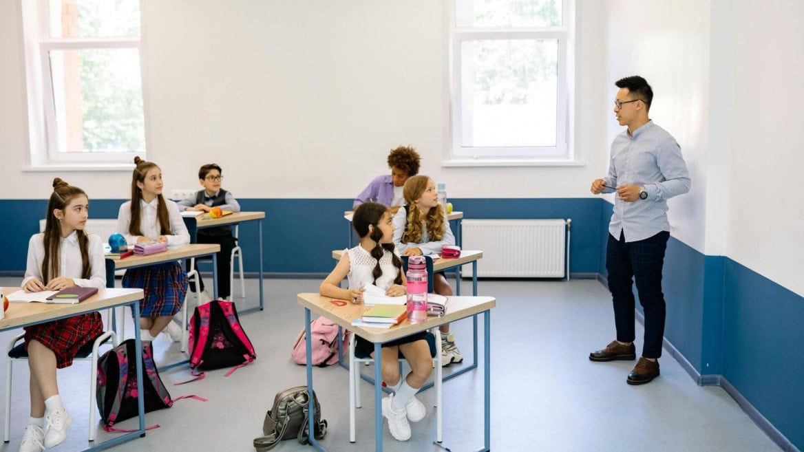 Salle de classe moderne et lumineuse avec enseignant, élèves en uniforme et tableau blanc.