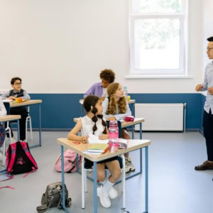 Salle de classe moderne et lumineuse avec enseignant, élèves en uniforme et tableau blanc.