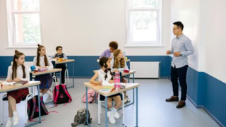 Salle de classe moderne et lumineuse avec enseignant, élèves en uniforme et tableau blanc.