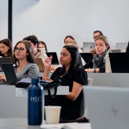 Salle de cours HEC Paris, étudiants attentifs, prise de notes et ordinateurs portables.