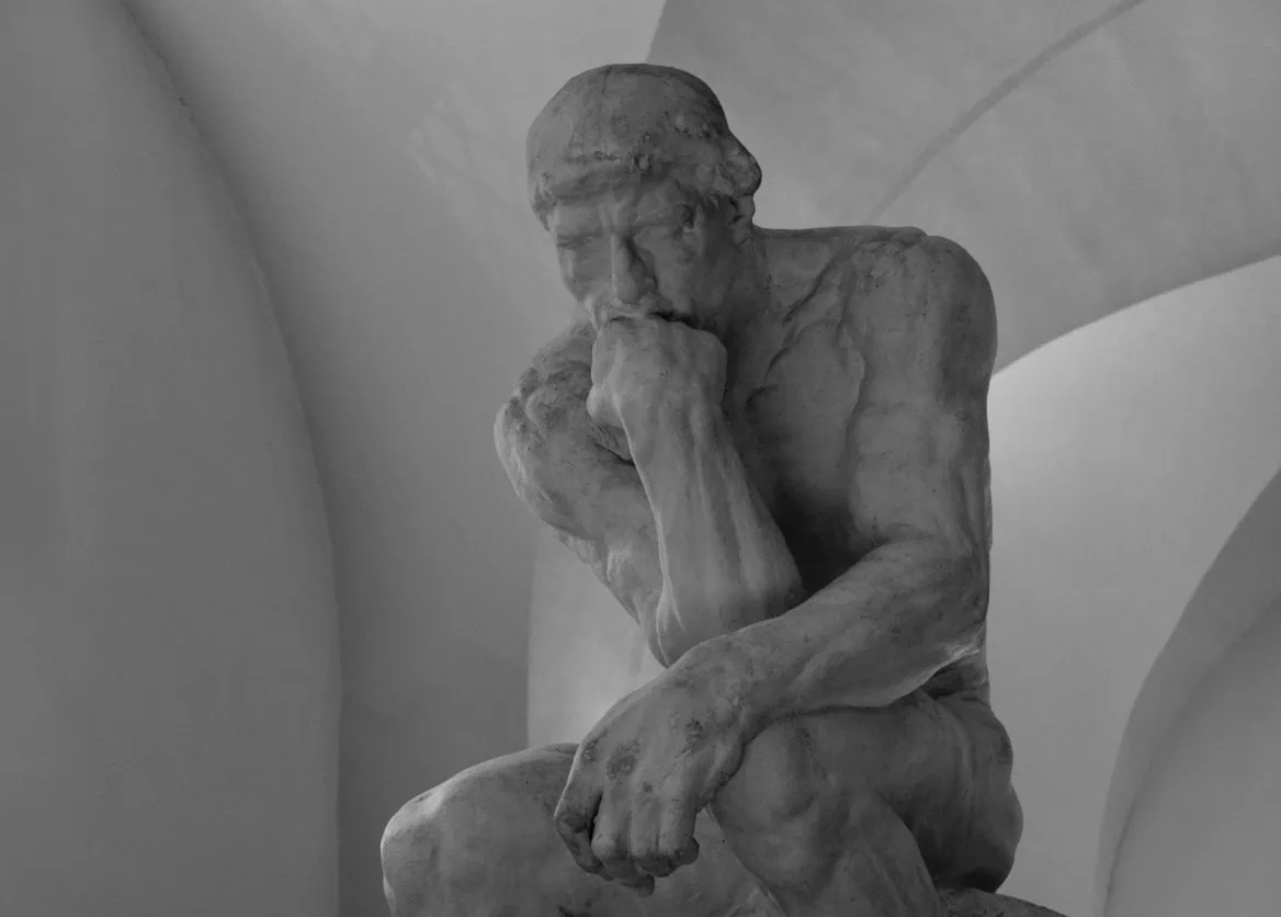 Sculpture dun penseur assis en pierre, mains jointes, portrait contemplatif en noir et blanc.
