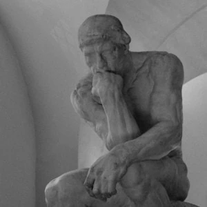 Sculpture dun penseur assis en pierre, mains jointes, portrait contemplatif en noir et blanc.