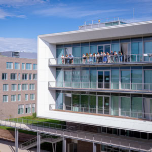 Bâtiment contemporain de campus avec balcon vitré en porte-à-faux et personnes sur terrasse.