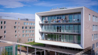 Bâtiment contemporain de campus avec balcon vitré en porte-à-faux et personnes sur terrasse.