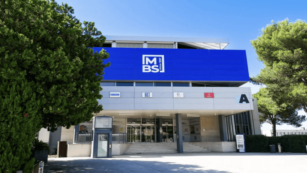 Entrée du bâtiment MBS: façade moderne, logo bleu, escalier et portes vitrées.