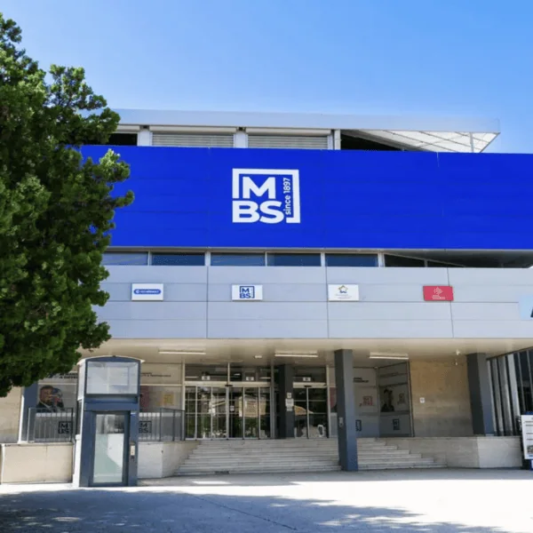 Entrée du bâtiment MBS: façade moderne, logo bleu, escalier et portes vitrées.