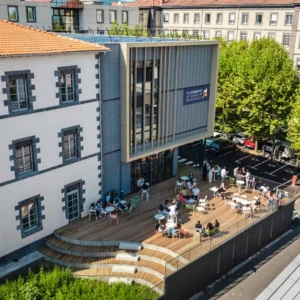 Terrasse ensoleillée du campus de Clermont École de Commerce, bâtiment historique et extension moderne.