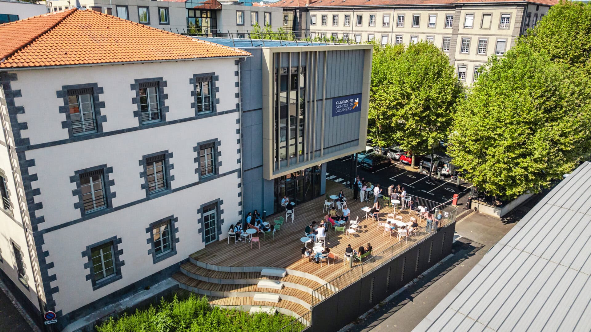 Terrasse ensoleillée du campus de Clermont École de Commerce, bâtiment historique et extension moderne.