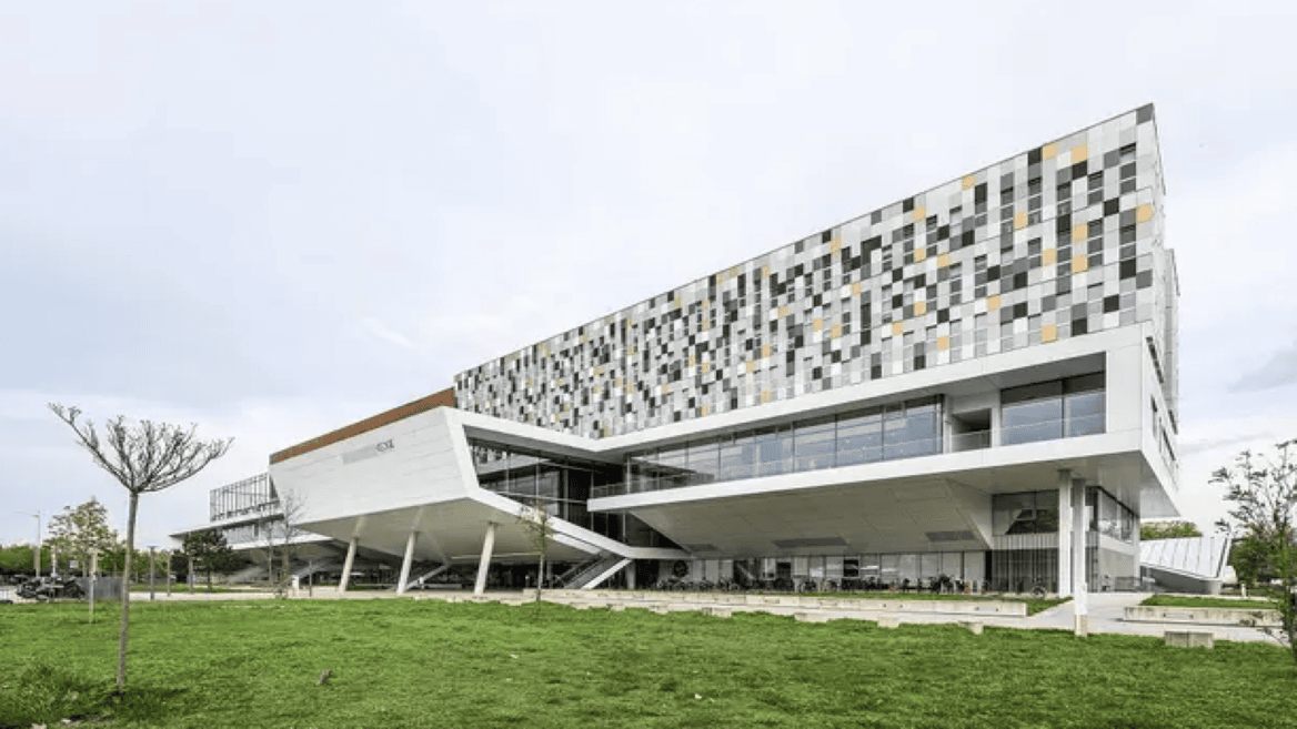 Bâtiment moderne à façade pixelisée en porte-à-faux, panneaux multicolores et base vitrée.