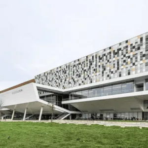 Bâtiment moderne à façade pixelisée en porte-à-faux, panneaux multicolores et base vitrée.