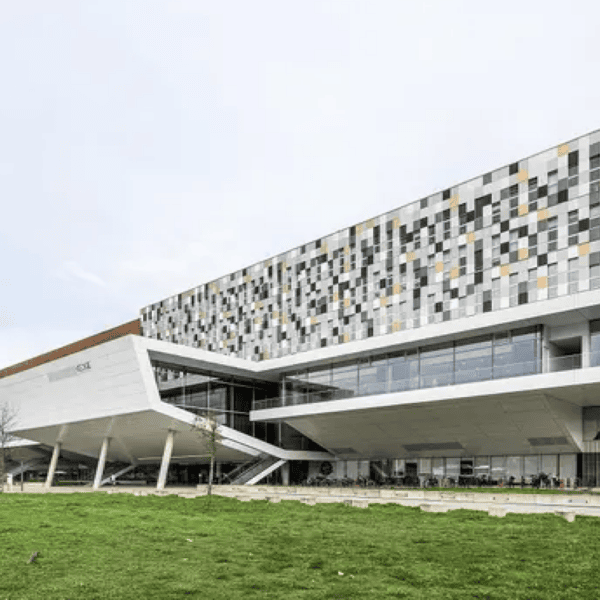 Bâtiment moderne à façade pixelisée en porte-à-faux, panneaux multicolores et base vitrée.