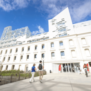 Bâtiment mixte pierre et verre, parvis et entrée animés par piétons et cycliste.