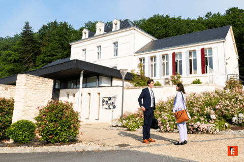 Bâtiment en pierre avec façade élégante, entrée moderne, jardins fleuris et professionnels en conversation.