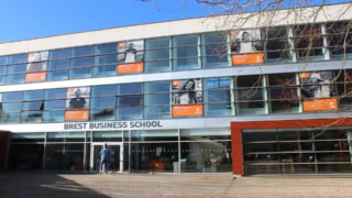 Façade moderne de Brest Business School avec entrée vitrée et affiches étudiantes.