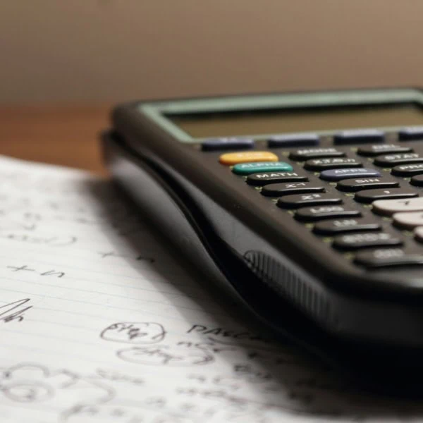 Calculatrice scientifique noire sur papier à lignes, notes manuscrites et calculs.
