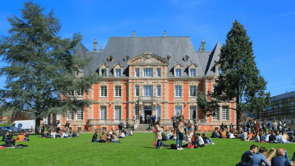 Pelouse de campus universitaire devant bâtiment en brique, étudiants qui se détendent.