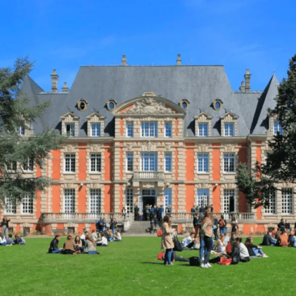 Pelouse de campus universitaire devant bâtiment en brique, étudiants qui se détendent.
