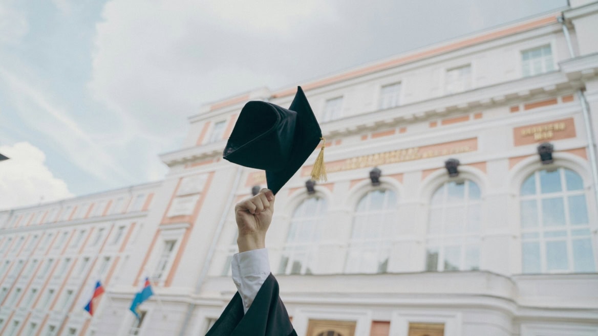 Toque de diplômé lancée au-dessus dune main devant un bâtiment universitaire classique.