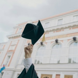 Toque de diplômé lancée au-dessus dune main devant un bâtiment universitaire classique.
