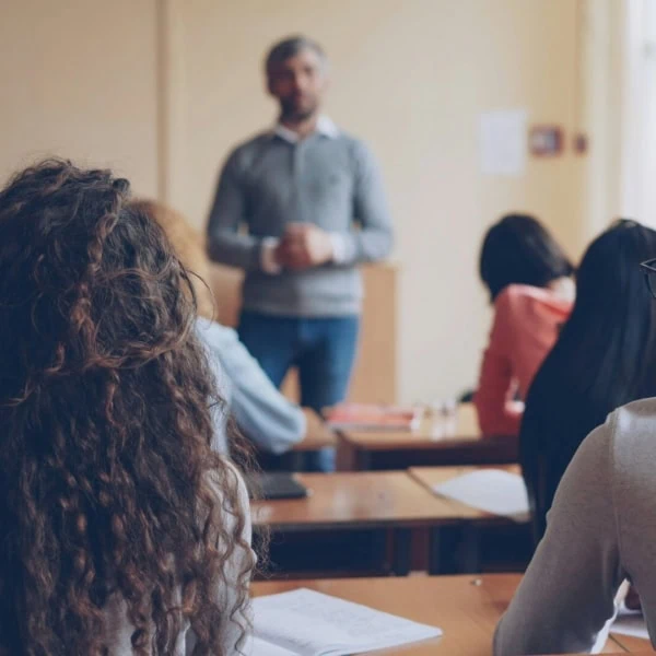 Classe avec élèves de dos, enseignant flou devant, prise de notes, lumière naturelle.
