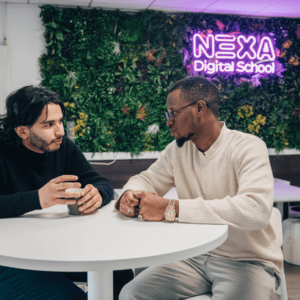 Deux hommes en conversation dans un espace coworking devant mur végétal et néon NEXA.