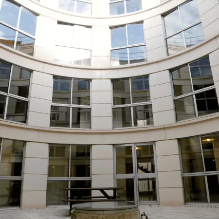 Cour intérieure moderne en pierre courbe avec façade vitrée répétitive, banc et fontaine.