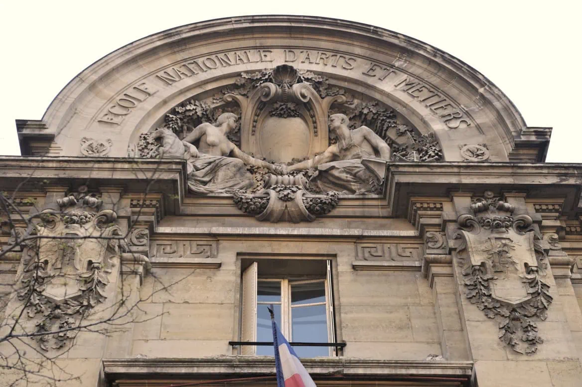 Façade de l’École Nationale dArts et Métiers, tympan sculpté en pierre, drapeau français.