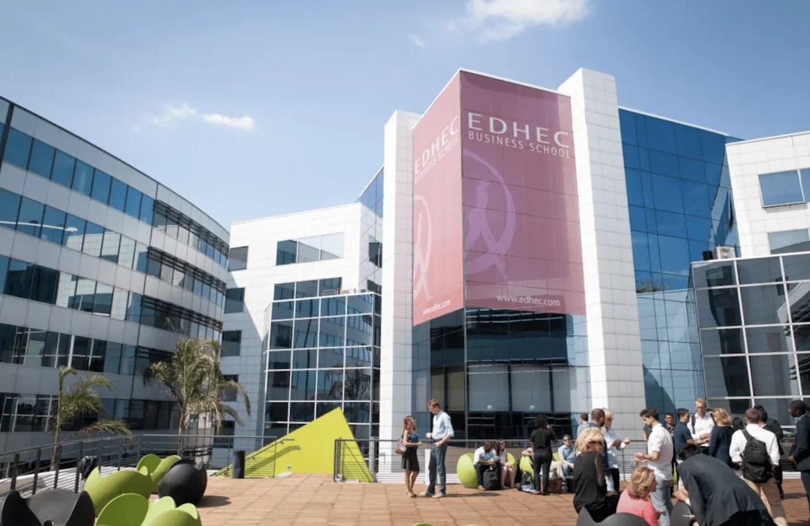Campus EDHEC moderne, terrasse ensoleillée avec étudiants, bâtiments vitrés et mobilier coloré.