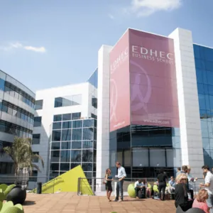 Campus EDHEC moderne, terrasse ensoleillée avec étudiants, bâtiments vitrés et mobilier coloré.