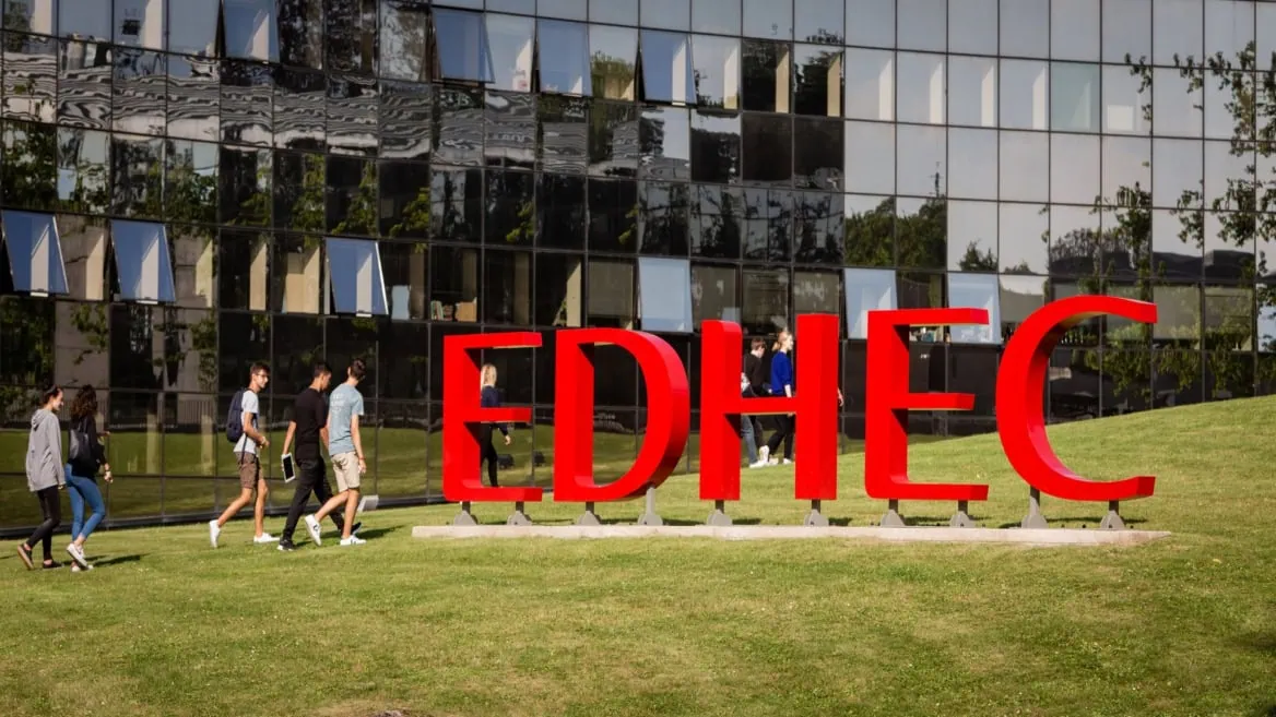 Signe rouge EDHEC sur pelouse de campus, étudiants en mouvement devant bâtiment vitré.