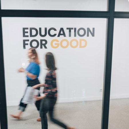 Affiche EDUCATION FOR GOOD sur mur blanc, couloir moderne, personnes floues en mouvement.