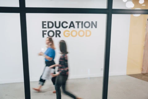 Affiche EDUCATION FOR GOOD sur mur blanc, couloir moderne, personnes floues en mouvement.