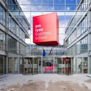 Façade moderne demlyon business school avec cube rouge et portes tournantes.