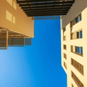 Architecture verticale entre bâtiments : façades sablées, lames métalliques, ciel azur et ombres géométriques.
