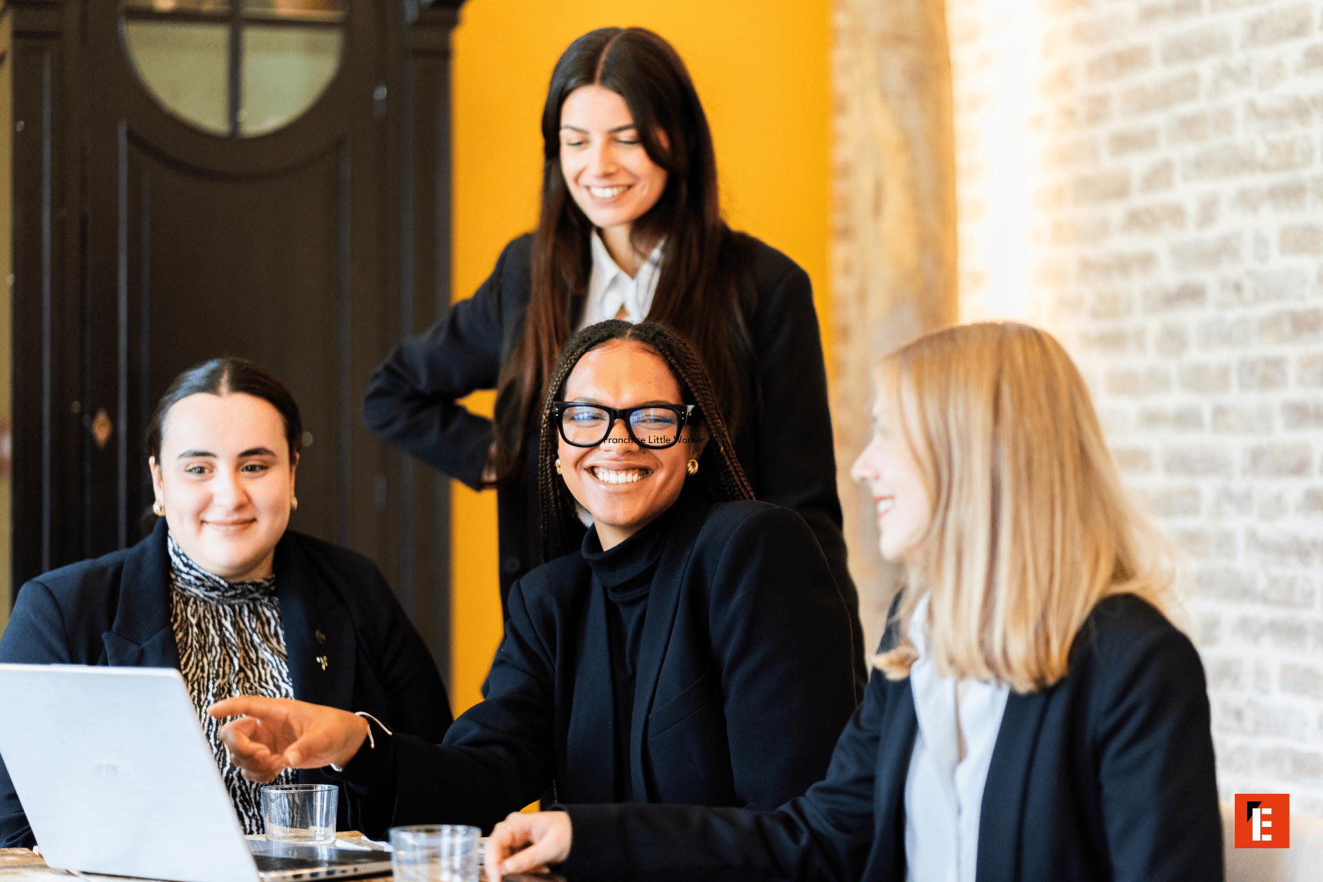 Équipe féminine en réunion collaborative autour dun ordinateur portable au bureau, sourires et travail déquipe.