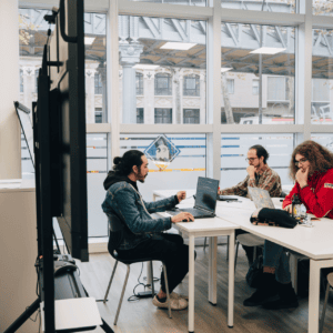 Espace de travail urbain collaboratif avec étudiants sur ordinateurs et lumière naturelle.