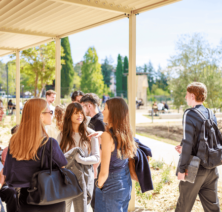 Étudiants en groupe discutant sur campus en plein air près dune allée couverte.