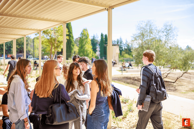 Étudiants en groupe discutant sur campus en plein air près dune allée couverte.
