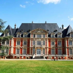 Façade de manoir en briques et pierre, toit dardoise, pelouse et arbres.