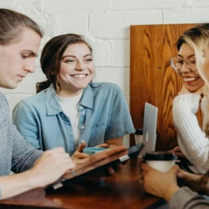 Groupe de jeunes autour dune table en bois, café, ordinateur portable, tablette.