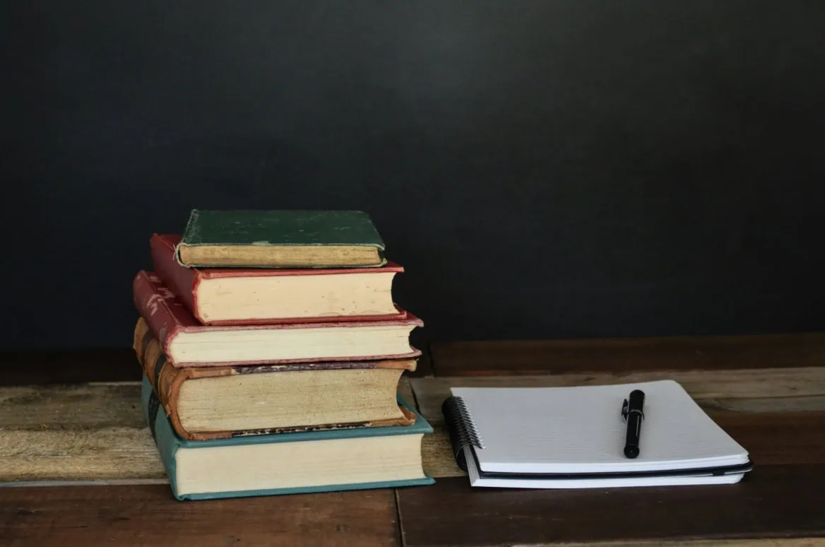 Livres anciens, cahier à spirales et stylo sur table en bois sombre.