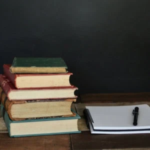 Livres anciens, cahier à spirales et stylo sur table en bois sombre.